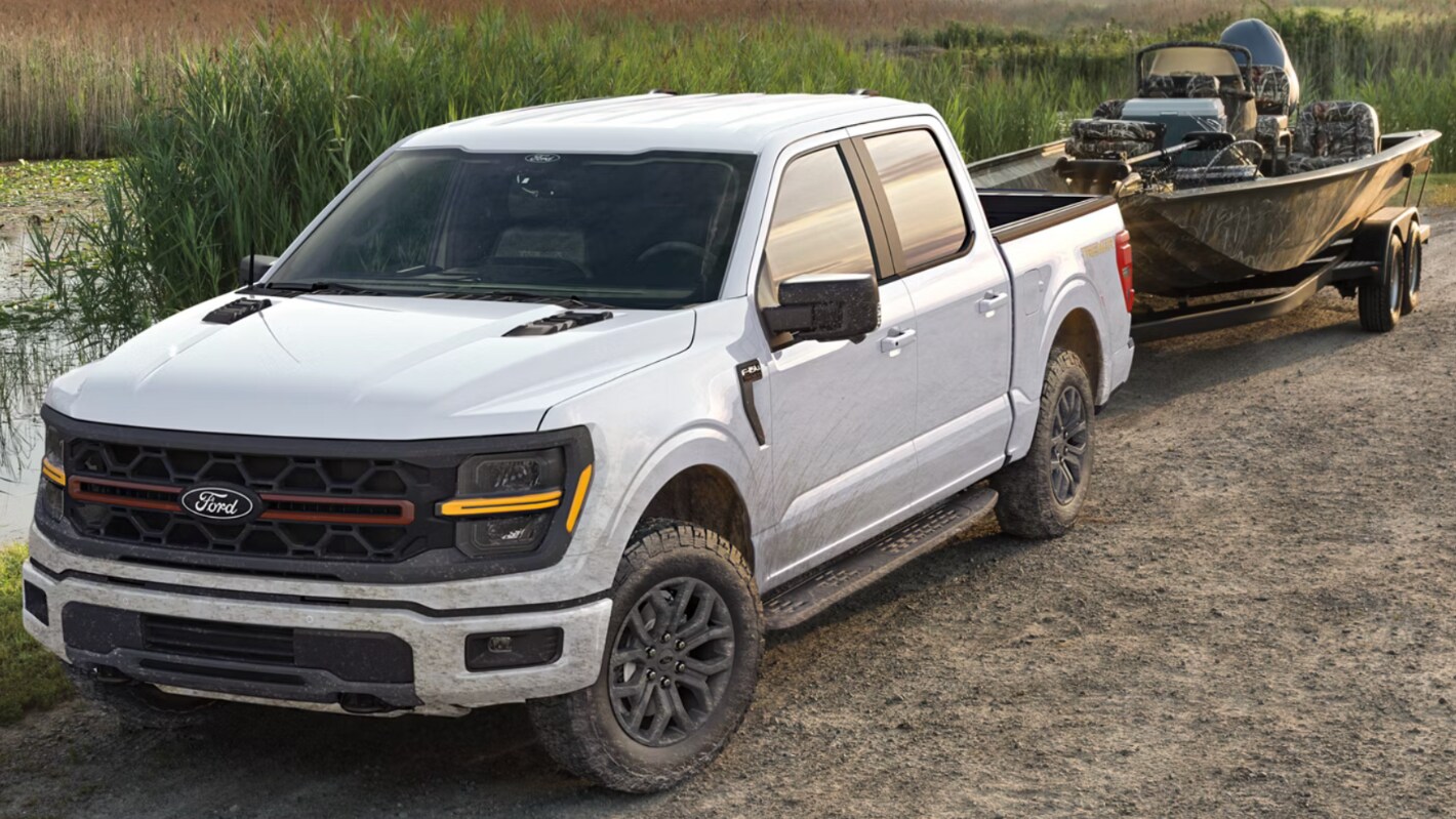 A white Ford F-150 towing a boat off-road by a swamp.