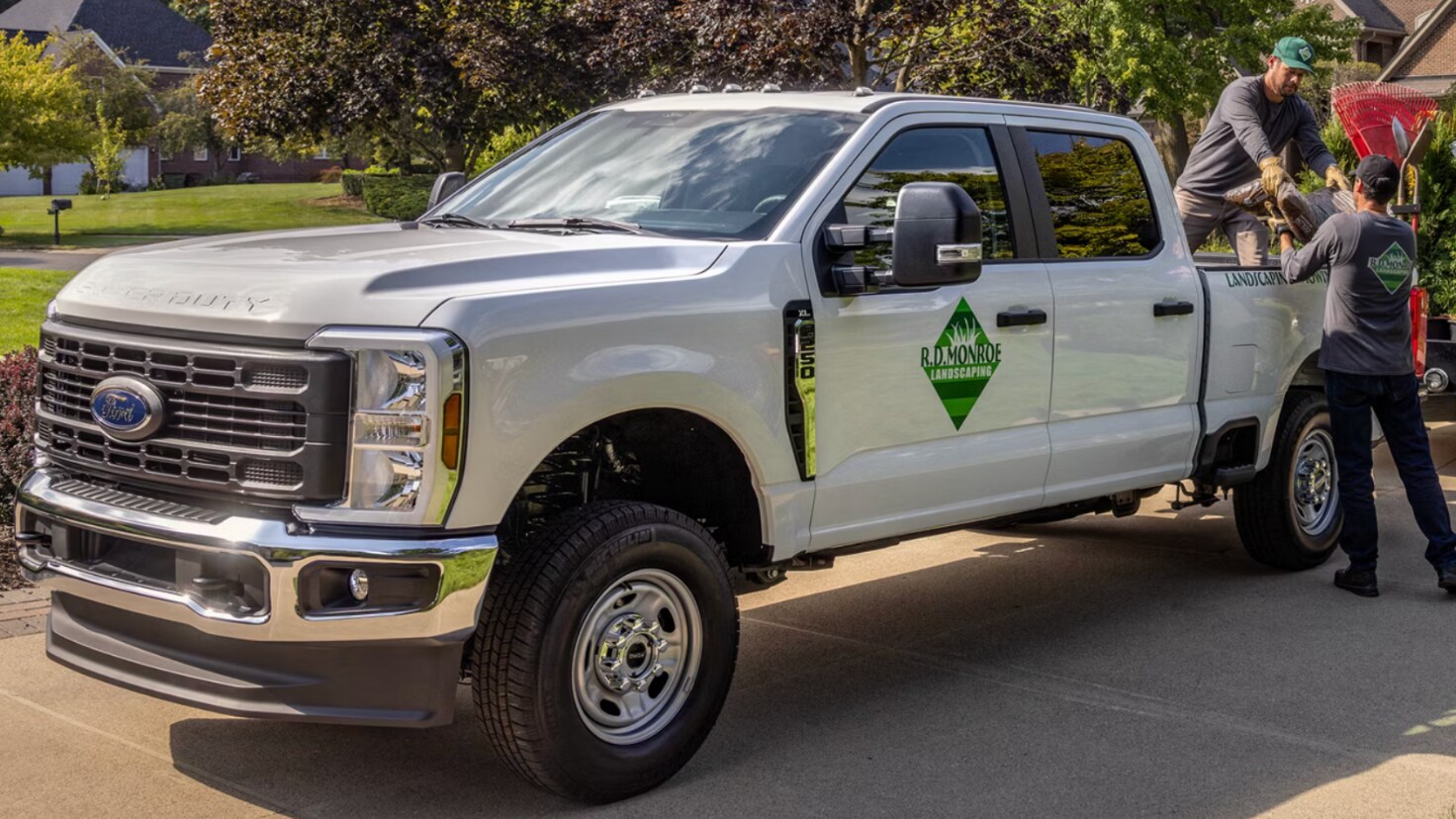 A silver heavy-duty Ford pickup being prepared to a pine tree and equipment in a driveway.