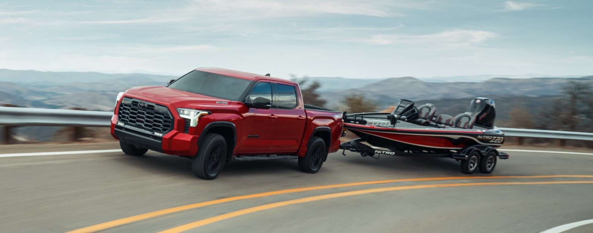 A red 2026 Toyota Tundra hauling a read boat as it turns along a curve. A red 2026 Toyota Tundra hauling a read boat as it turns along a curve.