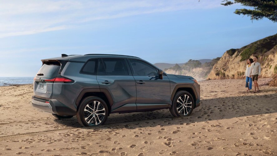 A gray Toyota RAV4 on a beach with a couple walking towards it.