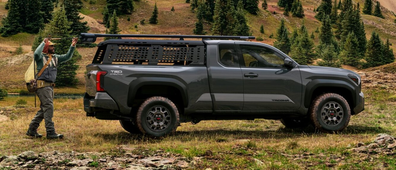 A black Toyota Tacoma in profile in a grassy area, with a man loading up its truck bed.