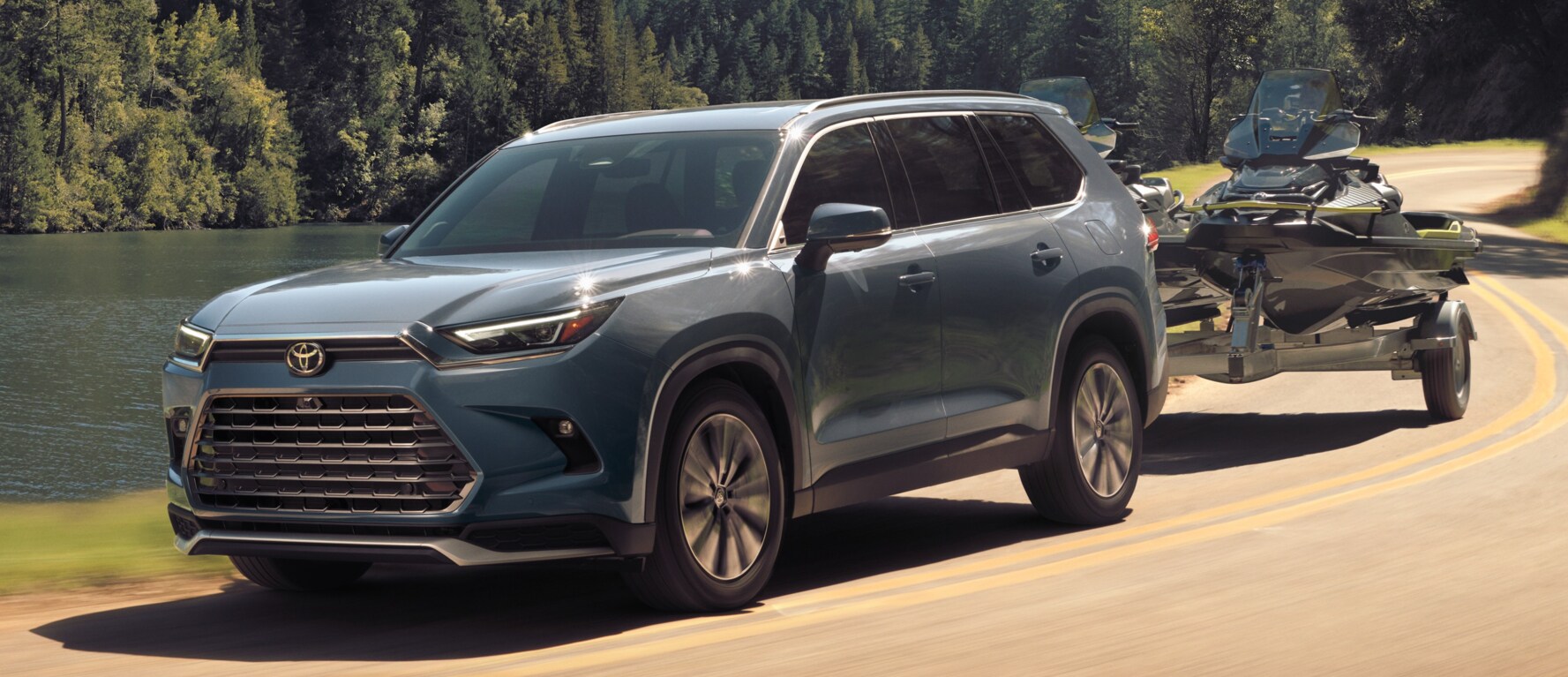 A light blue Toyota Grand Highlander driving down a road by a lake while towing a boat. A light blue Toyota Grand Highlander driving down a road by a lake while towing a boat.