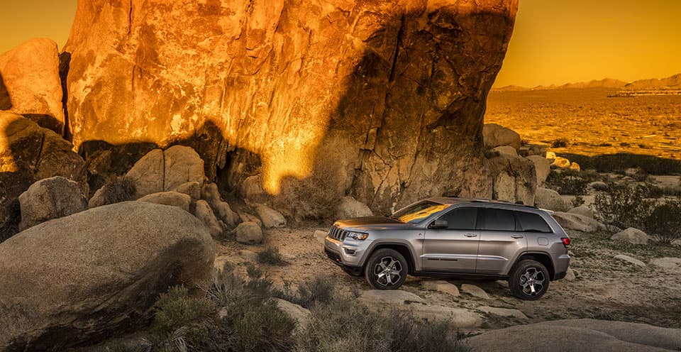 A silver 2019 Jeep Grand Cherokee Trailhawk at sunset near some large rocks
