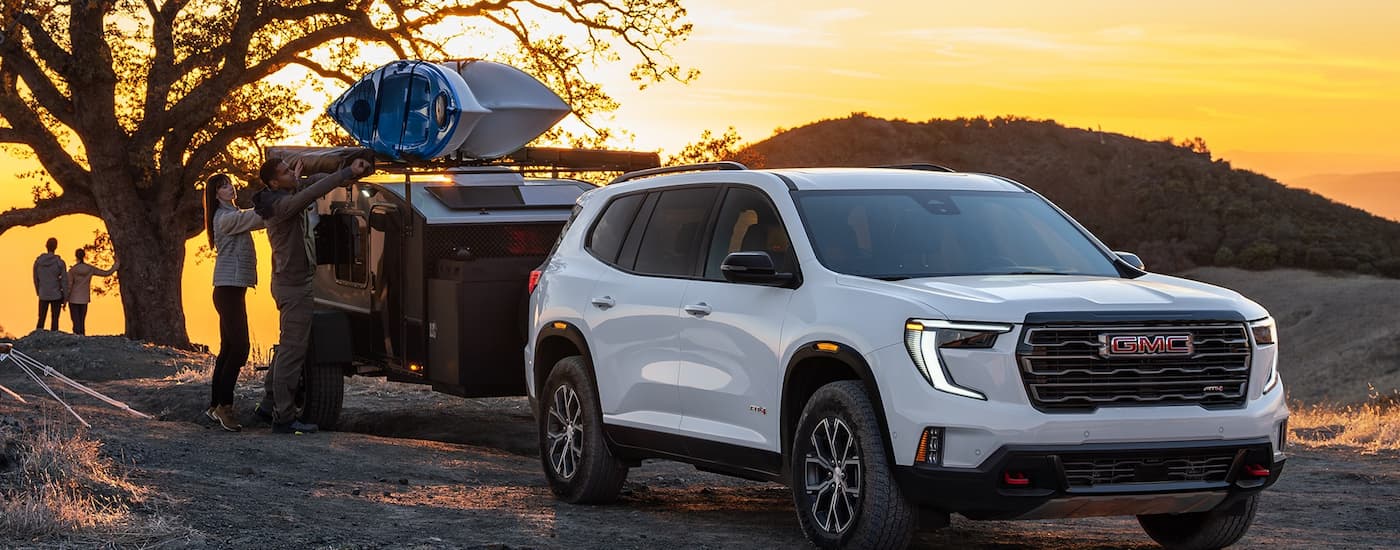 White 2026 GMC Acadia towing a trailer off-road.