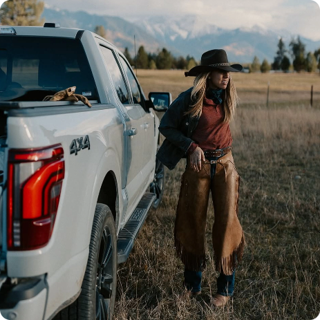 Woman in western attire standing beside a white Ford pickup truck in an open field, representing employee pricing offers