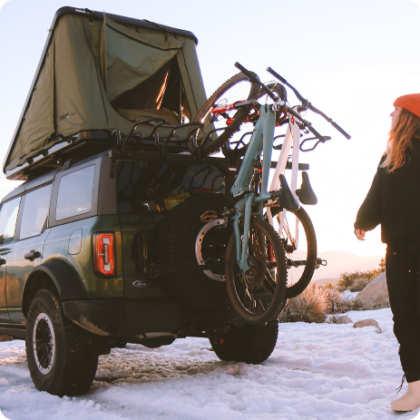 Ford SUV with rooftop tent and mounted bikes parked in a snowy landscape with person walking nearby, representing employee pricing offers