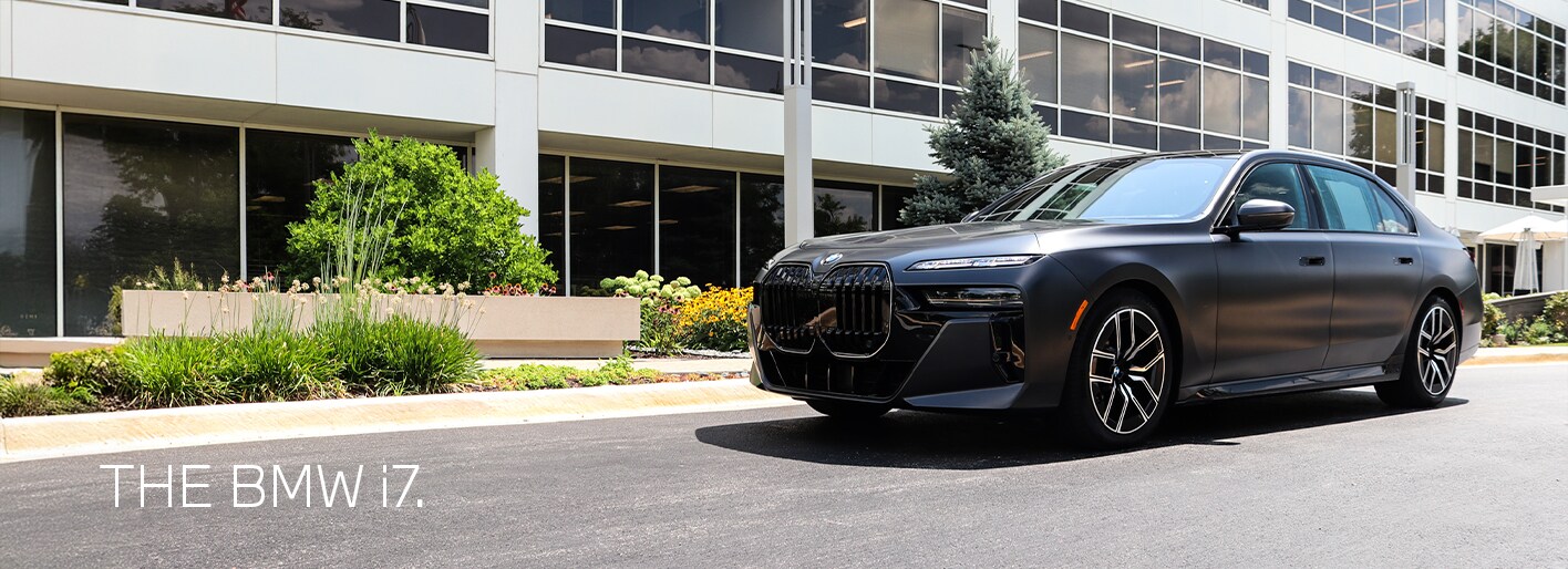 2026 BMW i7 luxury electric sedan parked on a scenic road, showcasing its sleek design, signature kidney grille, and modern LED headlights.