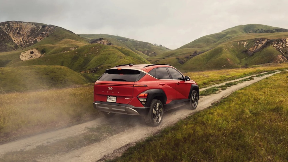 A red 2027 Hyundai Kona SUV driving along a dirt trail