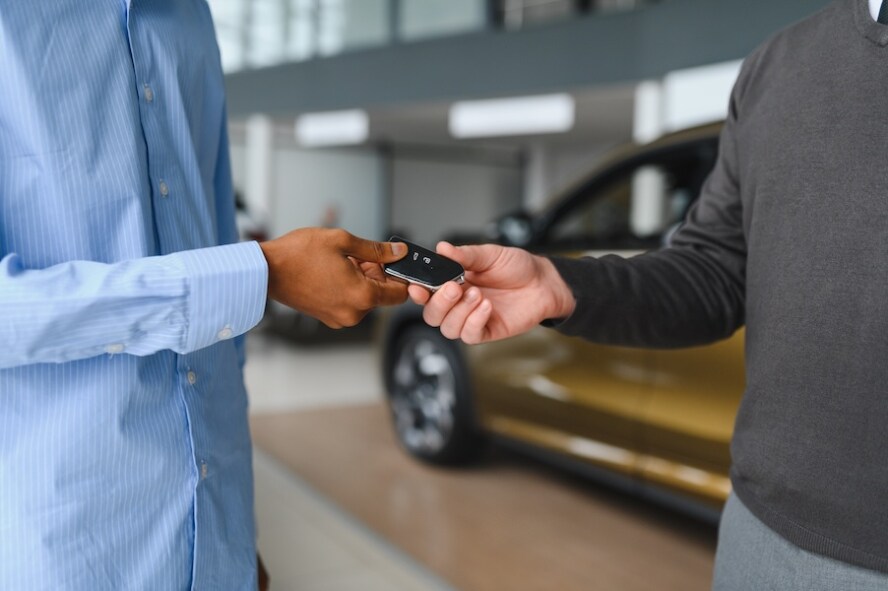 A car salesman handing a customer a car key inside a car dealership