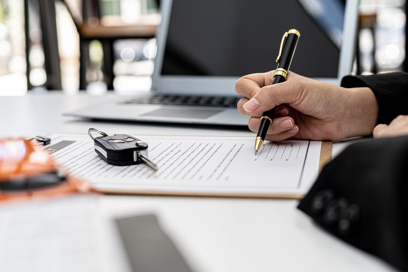 Close up of a hand signing financial paperwork with a car key on top of the document