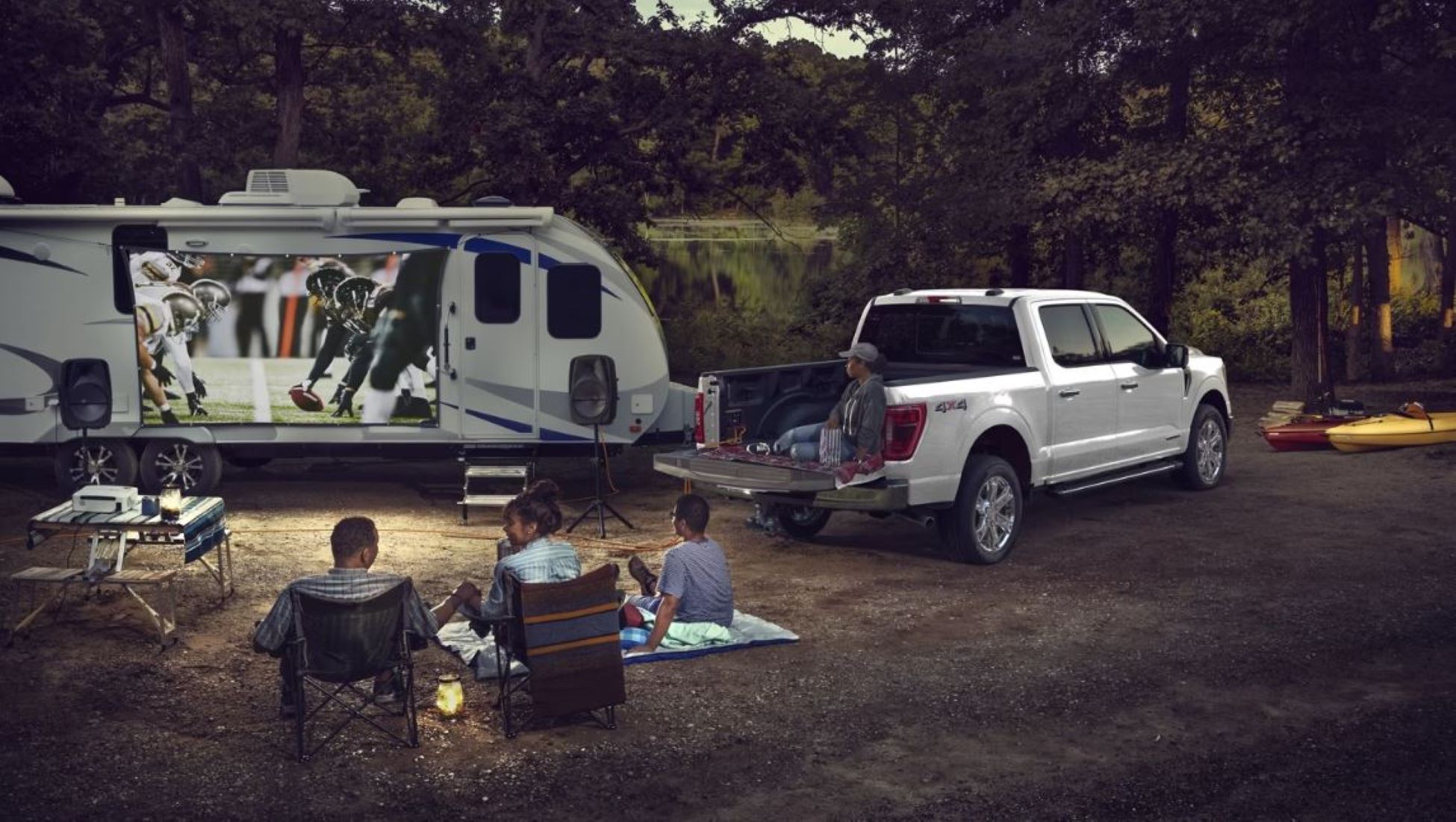 1 F-150 Camping.JPG A Ford F-150 pulling a camper parked with a family watching a movie projected onto a screen.