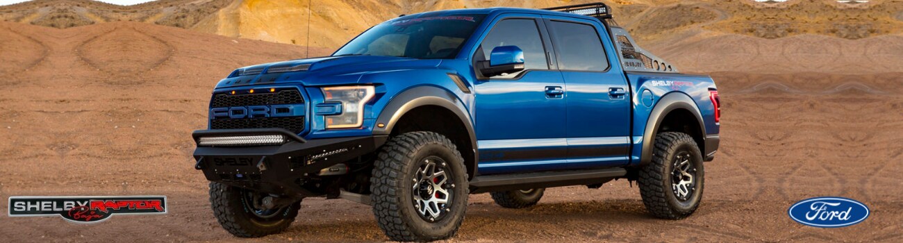 2018 Shelby Baja Raptor Phil Long Ford Chapel Hills Colorado Springs (1).png A blue 2018 Shelby Baja Raptor parked in some dirt and sand in a desert scene with off-road hills
