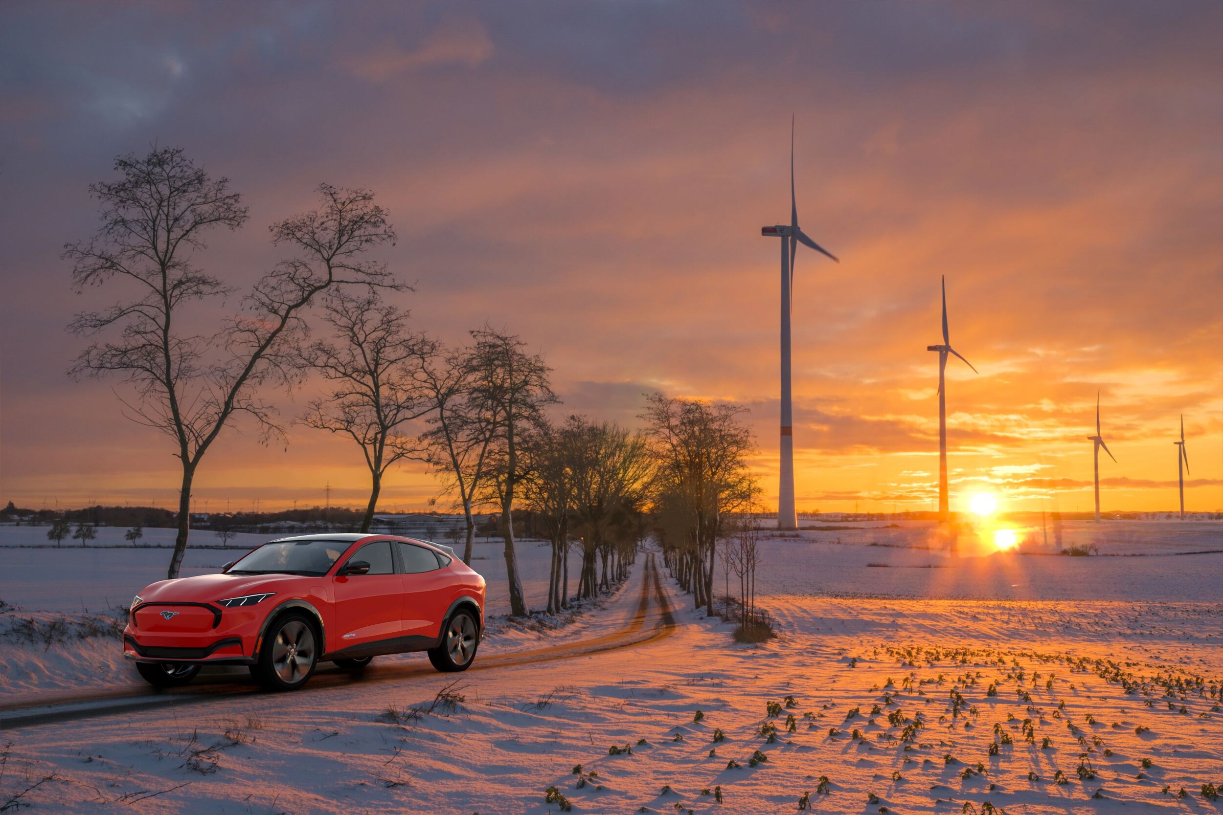 Mustang Mach E In Snow.jpeg A Mustang Mach-E Driving across a snowy field with windmills in the background.