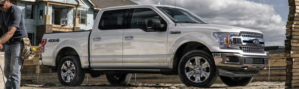 2019 Ford F-150 Truck in Colorado Springs at Phil Long Ford.png Passenger side angle of a white 2019 Ford F-150 work truck parked on a home constructions site with piles of lumber and a construction worker in the foreground