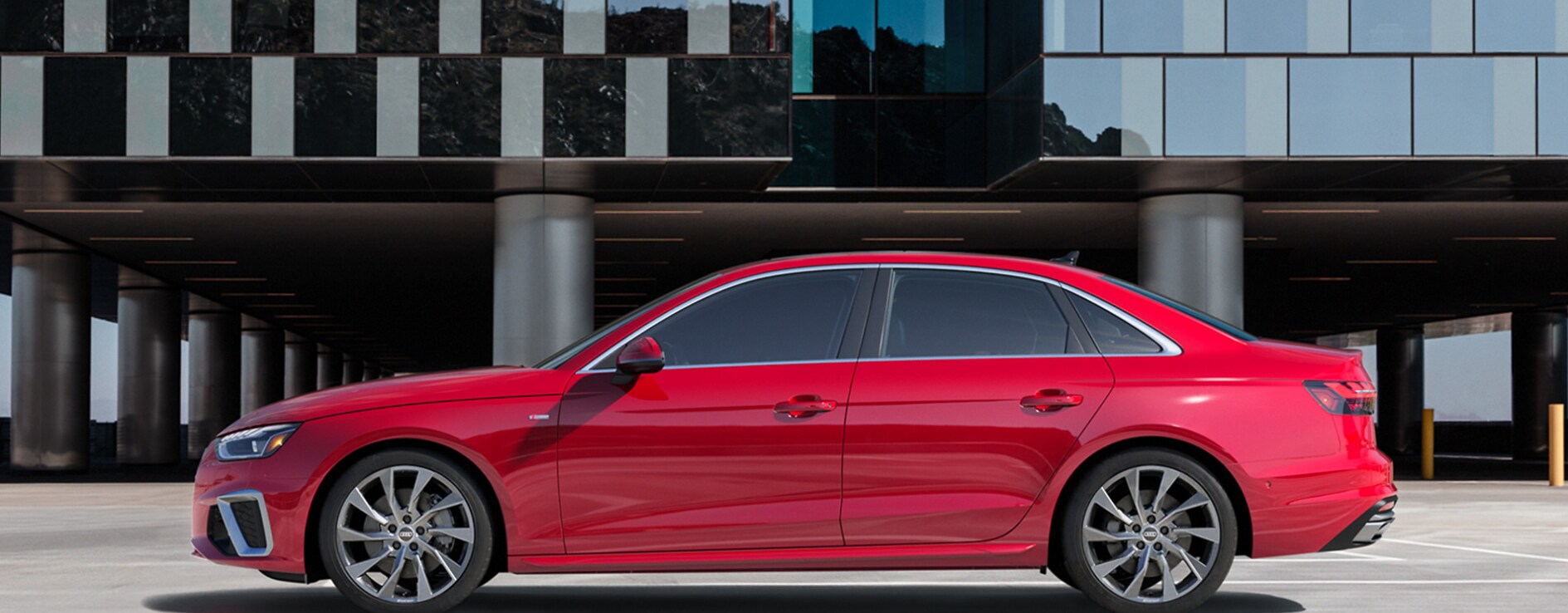 2023-audi-a4-3.PNG A profile view of a red 2023 Audi A4 parked in front of a city building