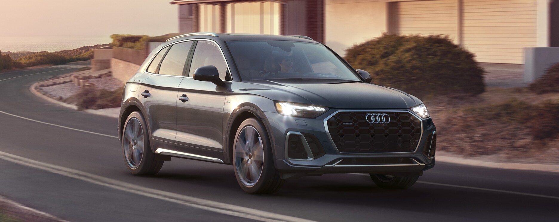 2023-Audi Q5 TFSI E -1.PNG A dark gray 2023 Audi Q5 TFSI e takes a turn at sunset on a road