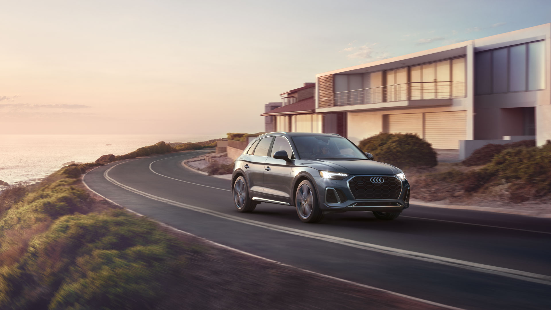 1920x1080_v1_MY24_-_Q5_TFSIe_-_Side_Profile_-_Driving_1.jpg An Audi Q5 driving on a costal road.