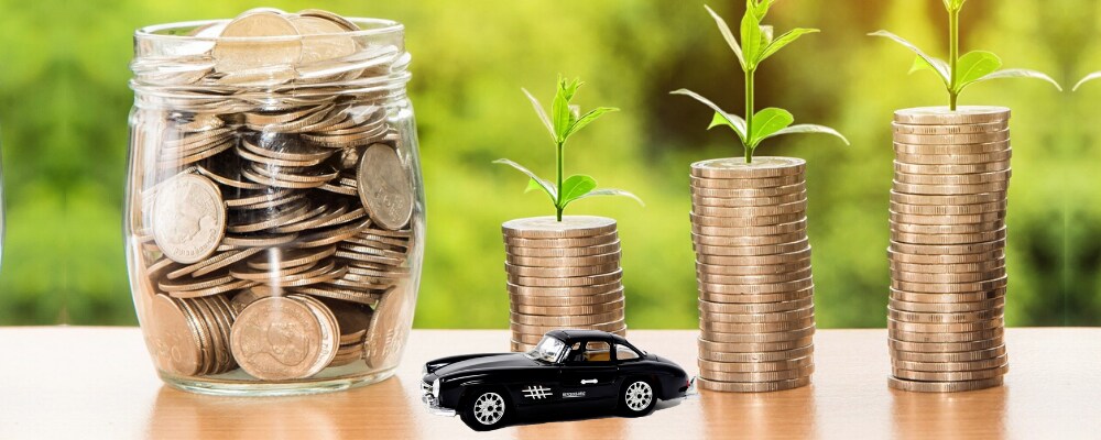 How to Finance Used Cars (1).png Stacks of coin money on a hardwood table top with a black Mercedes-Benz toy car sitting in front