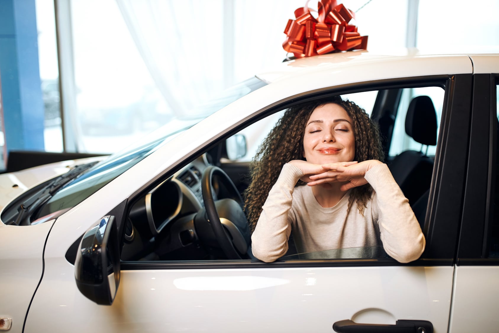 Picture8.png A woman sits in the drivers seat with a big smile facing out the window in a car with a christmas bow on top