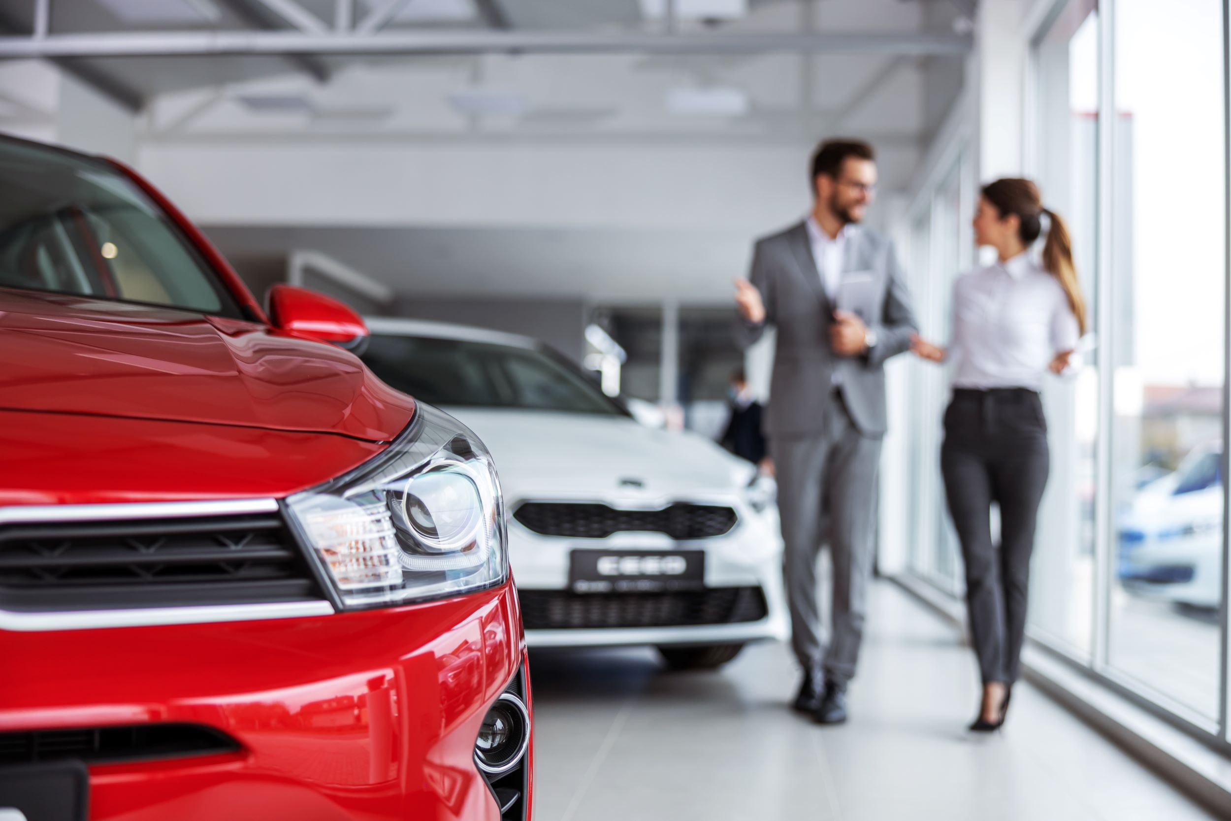 AdobeStock_409406174.jpeg Two people discussing the details of a car inside a car dealership.