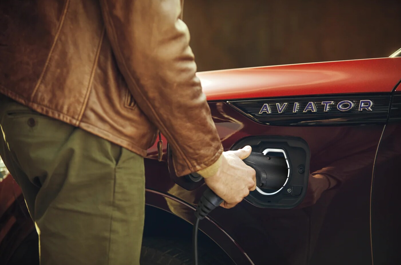 EV-Charging-Station-5.PNG A closeup of a man as he connects a charger to a red 2022 Lincoln Aviator electric hybrid plugin
