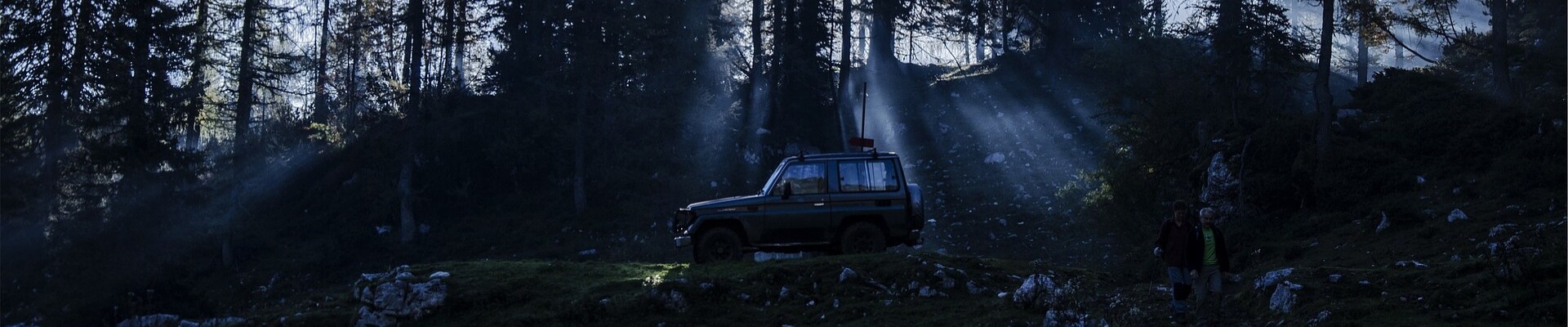 Best used 4x4 SUVs in Colorado Springs Phil Long Dealerships.png Distant view of a used 4x4 SUV parked on a rocky cliff inside a shaded forest as sunlight breaks through the trees