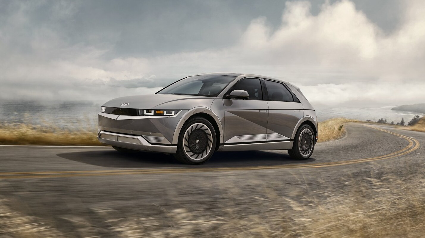 2022-Hyundai-Ioniq-5-2.png A silver 2022 Hyundai Ionic 5 electric vehicle is shown speeding down a curving highway nex to a large body of water with a blurred foreground and clouds and an overcast look to the sky in the background