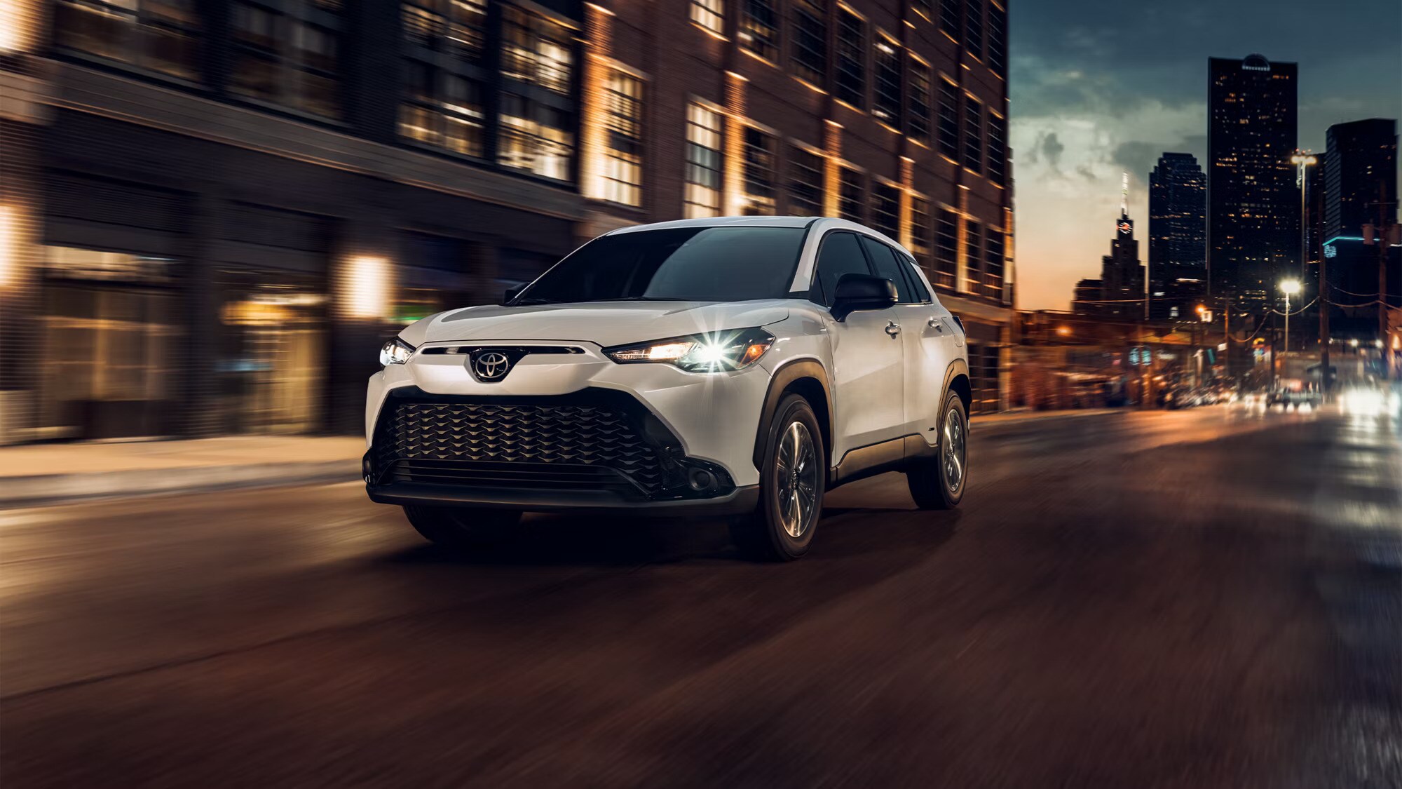 2024%20Corolla%20Cross.jpg A white 2024 Toyota Corolla Cross speeding down a city road at night.