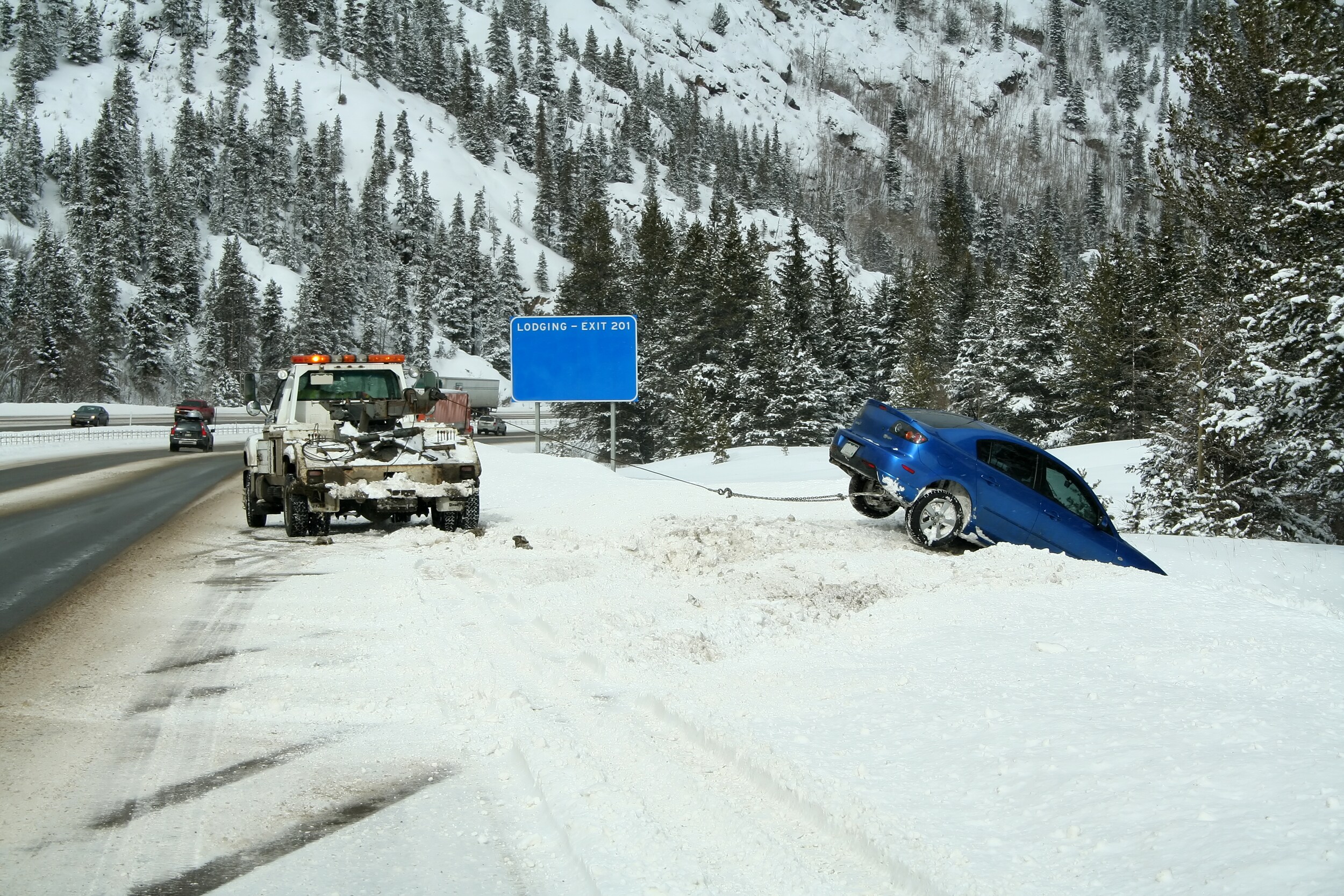 Winter%20Tires%20Safe%20Driving.jpeg A tow truck pulling a blue car off the side of the snowy mountain road.