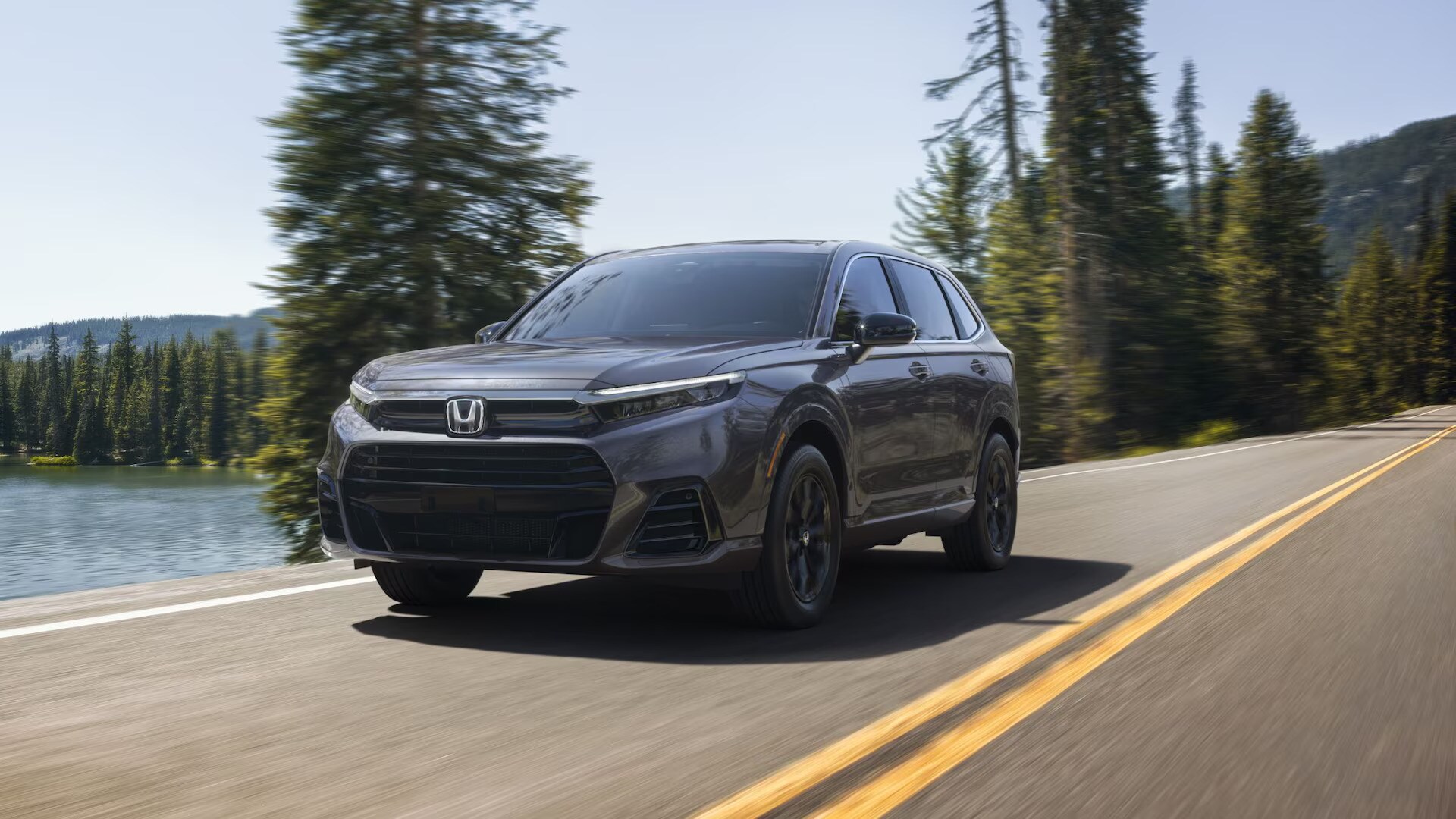 2025%20HondaCR-V-FCEV.jpg A grey new 2025 Honda CR-C FCEV driving on a forest highway during the day with trees and a lake in the background.