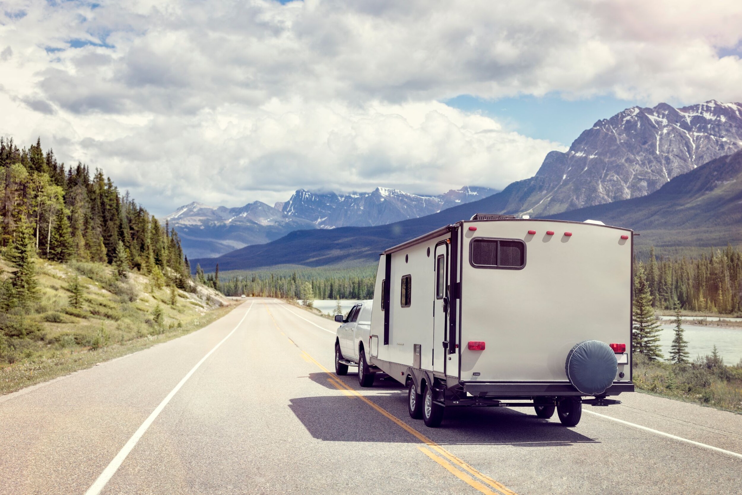 AdobeStock_120877296.jpeg A truck pulling a camper down a mountain valley road.