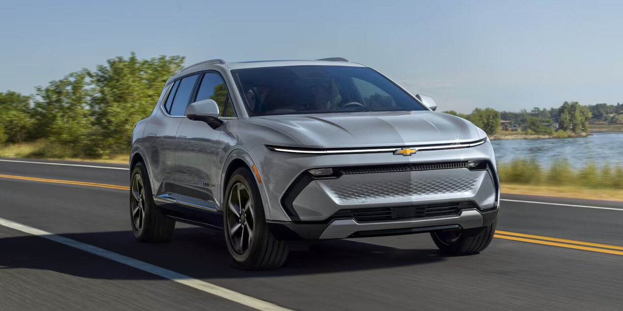 2025%20Chevy%20Equinox.jpg A blue new 2025 Chevrolet Equinox EV driving on a highway during the day with a tree and a lake in the background.
