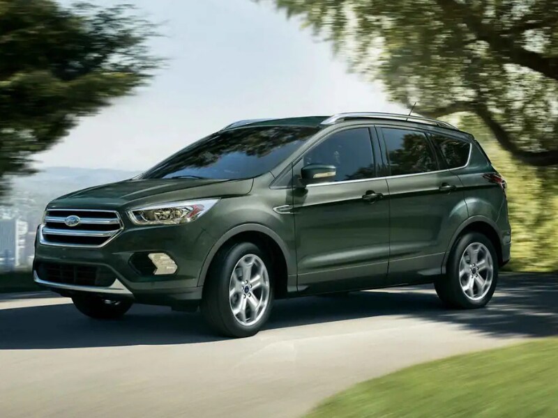 Front Side Exterior of a dark green 2019 Ford Escape driving around a curve through some trees