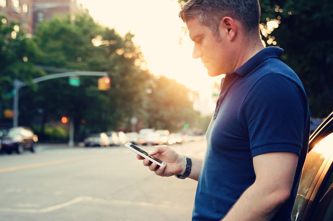 roadside assistance.JPG A man leans on his car parked on the street while using his cellphone