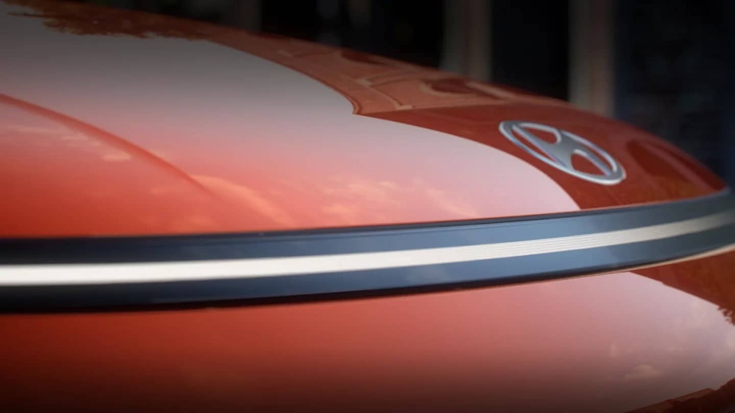 Close-up of the full-width front light bar and Hyundai logo on an orange 2027 Hyundai Kona