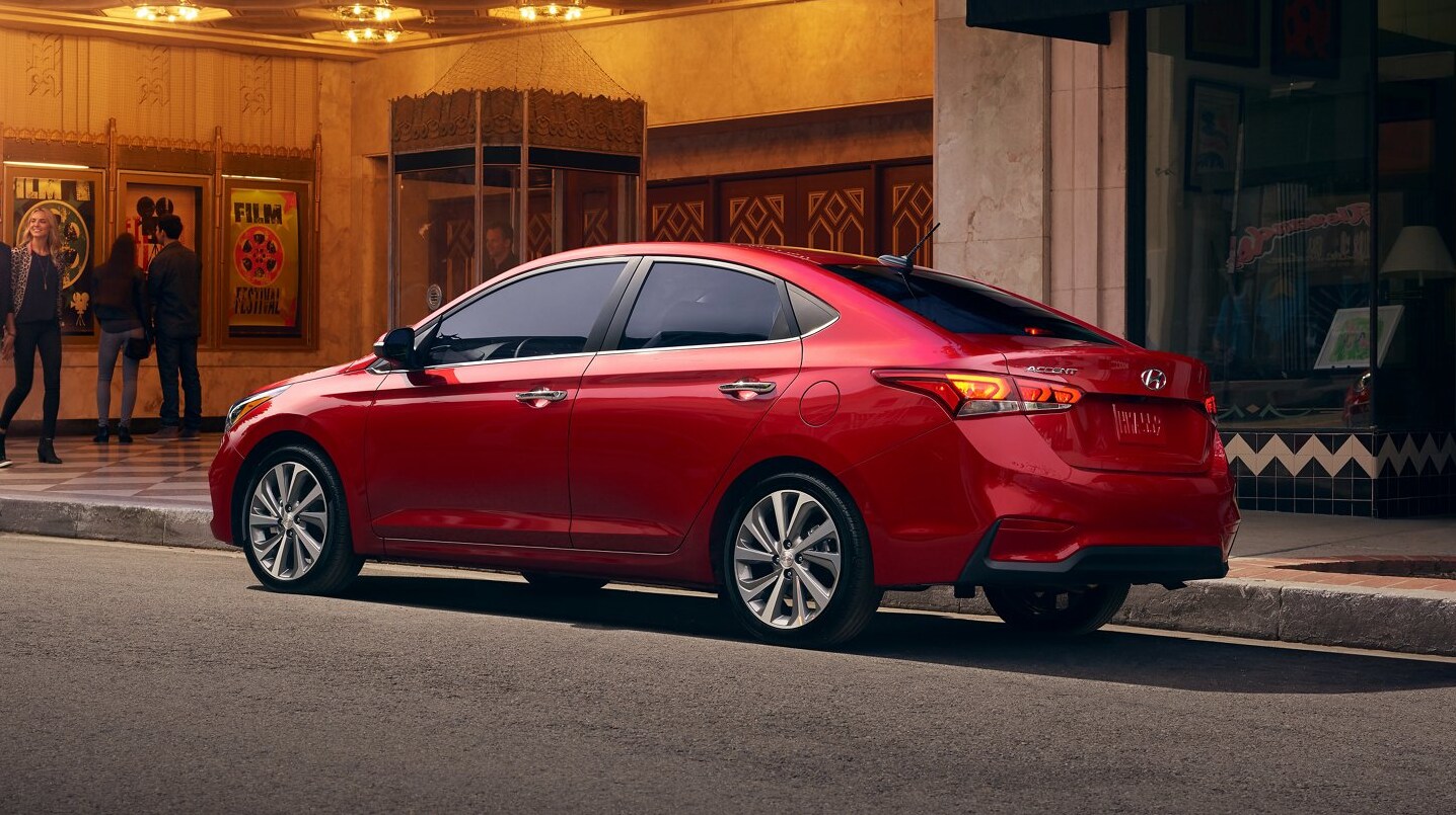 A red 2022 Hyundai Accent sits parked in front of a city movie theater on an angle showing the profile and back of the car