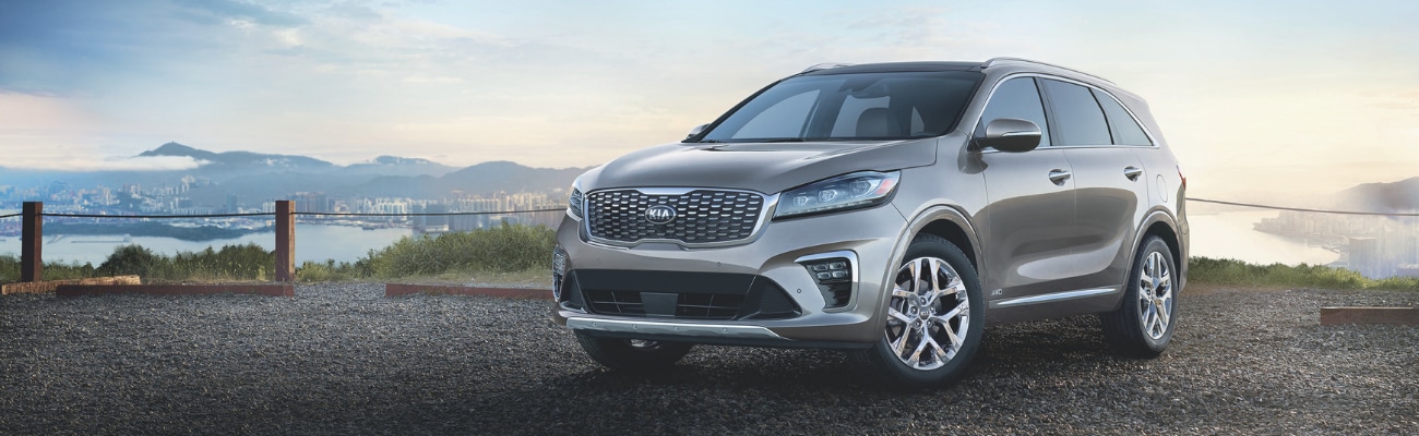 Driver side view of a 2019 Kia Sorento parked on a rocky cliff roped off on the edge overlooking a city at sunset