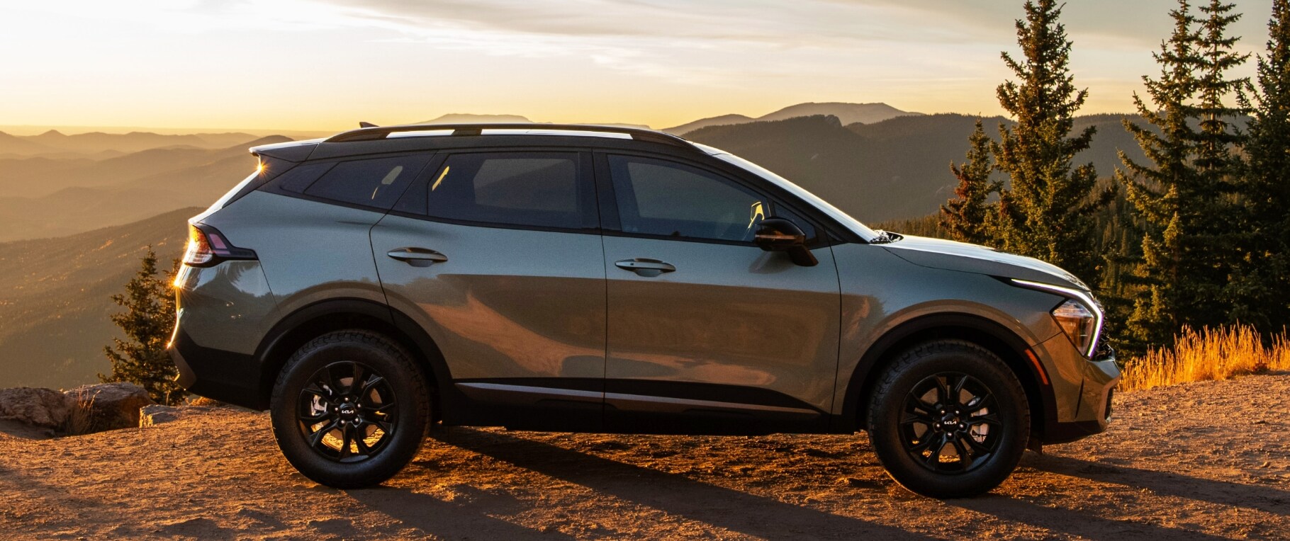 Kia Sportage 1.PNG A metallic silver 2023 Kia Sportage in profile view parked in front of a sunset