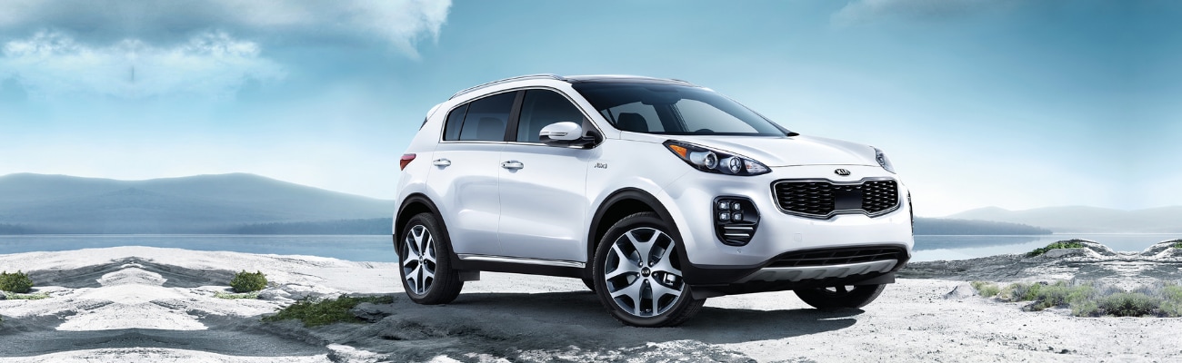 Front passenger side view of a white 2019 Kia Sportage SUV sitting at the top of a cliff overlooking a hazy mountain range Front passenger side view of a white 2019 Kia Sportage SUV sitting at the top of a cliff overlooking a hazy mountain range