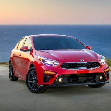 2019kiaforteincoloradospringsatphillongkia A still frame shot of a red 2019 Kia Forte parked on a concrete slab overlooking a vast blue ocean and an orange colored sky