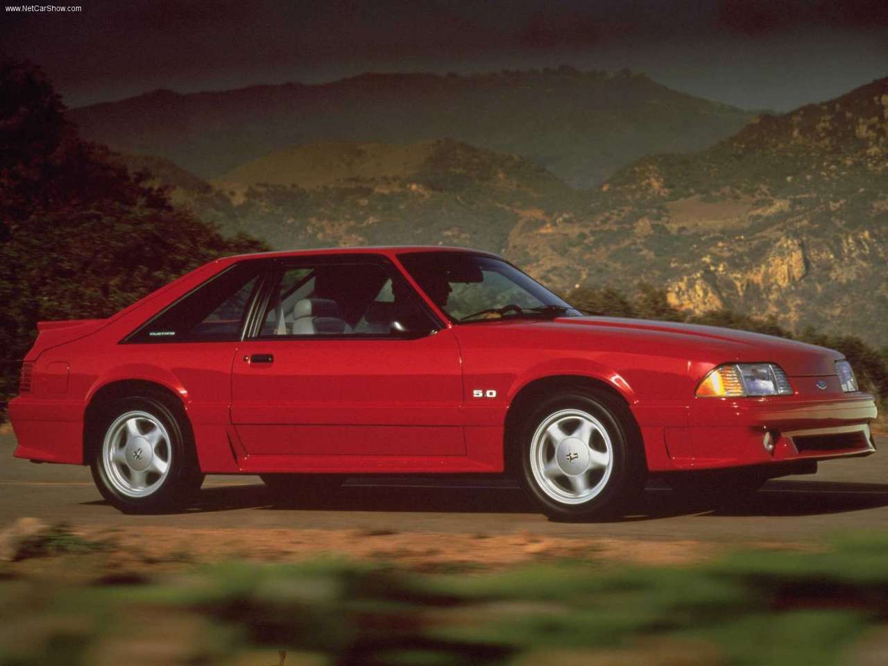 Ford-Mustang-1991-1280-01.jpg A red 1991 third generation Ford Mustang driving through a mountain road.