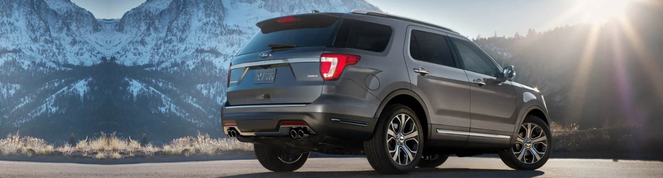 2019 Ford Explorer configurations in Colorado Springs Phil Long Ford Motor City.png Rear passenger side of a dark gray 2019 Ford Explorer parked on the side of a road at the base of a snowy mountain range as the sun sets behind the mountains