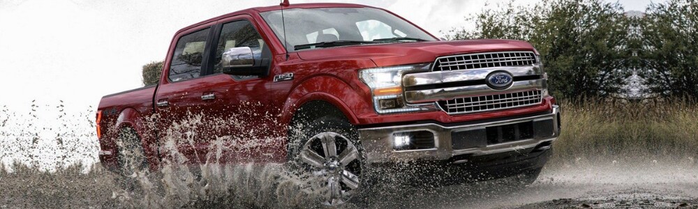 2019 Ford F-150 Truck in Colorado Springs at Phil Long Ford Motor City.png Angle of the passenger side of a ruby red 2019 Ford F-150 driving through a puddle with muddy water splashing onto the side of the Ford truck on a cloudy day