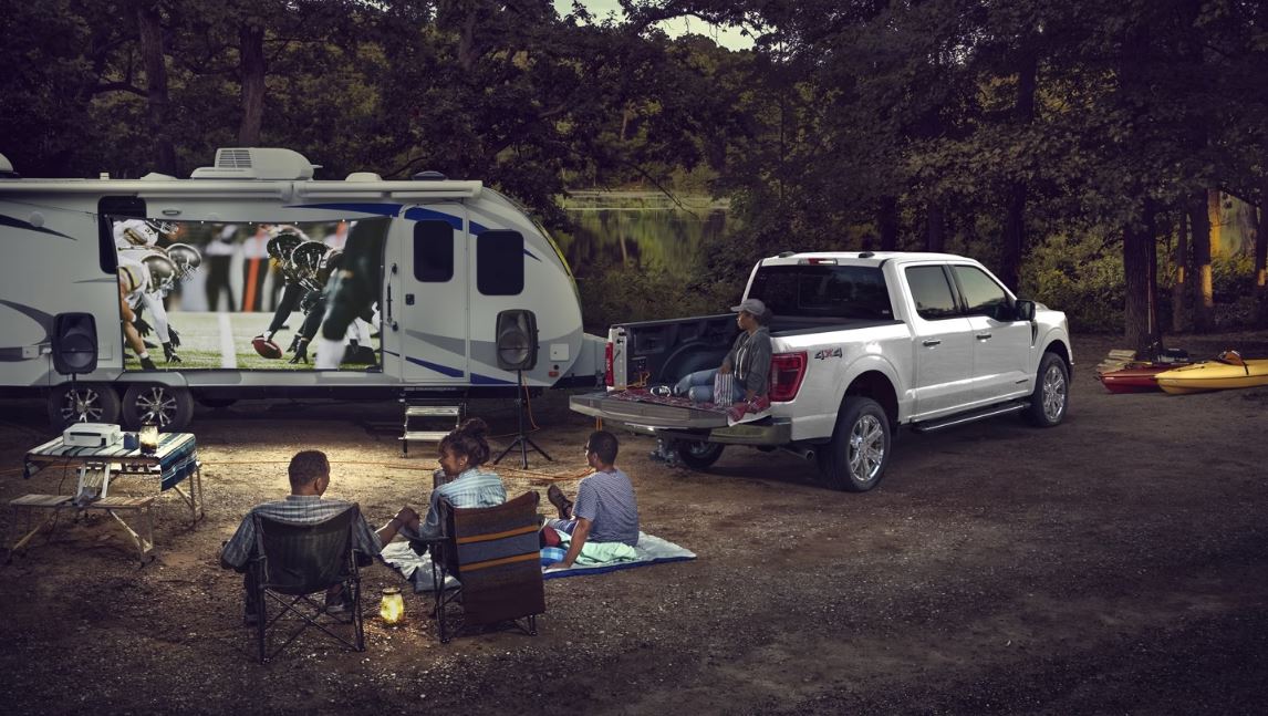 A Ford F-150 parked at a campsite with a projector showing a movie.