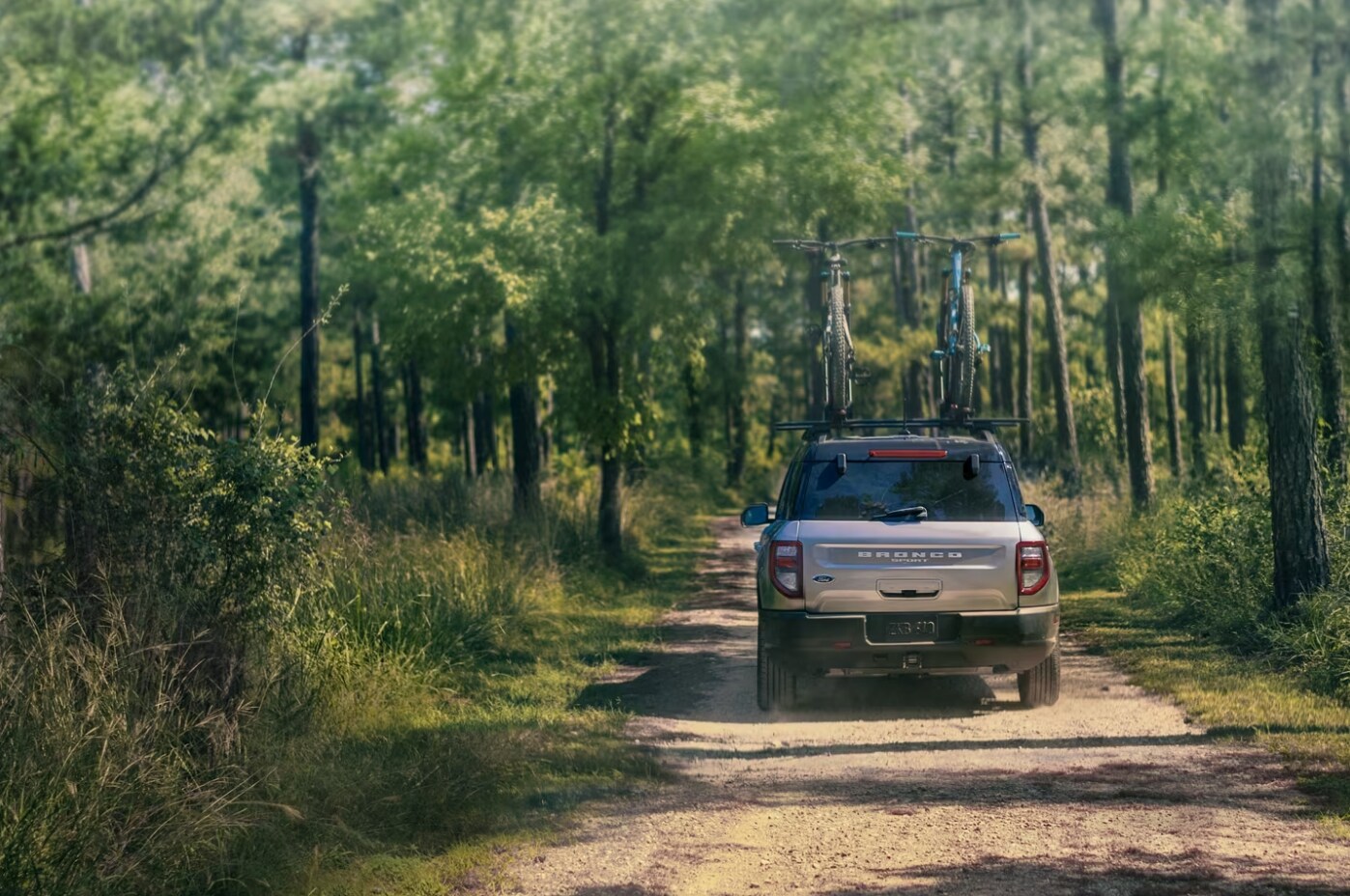 2023-bronco-sport-outer-banks-2.PNG A view of the back of a 2023 Ford Bronco Sport Outer Banks Edition as it drives down a dirt road in a forest