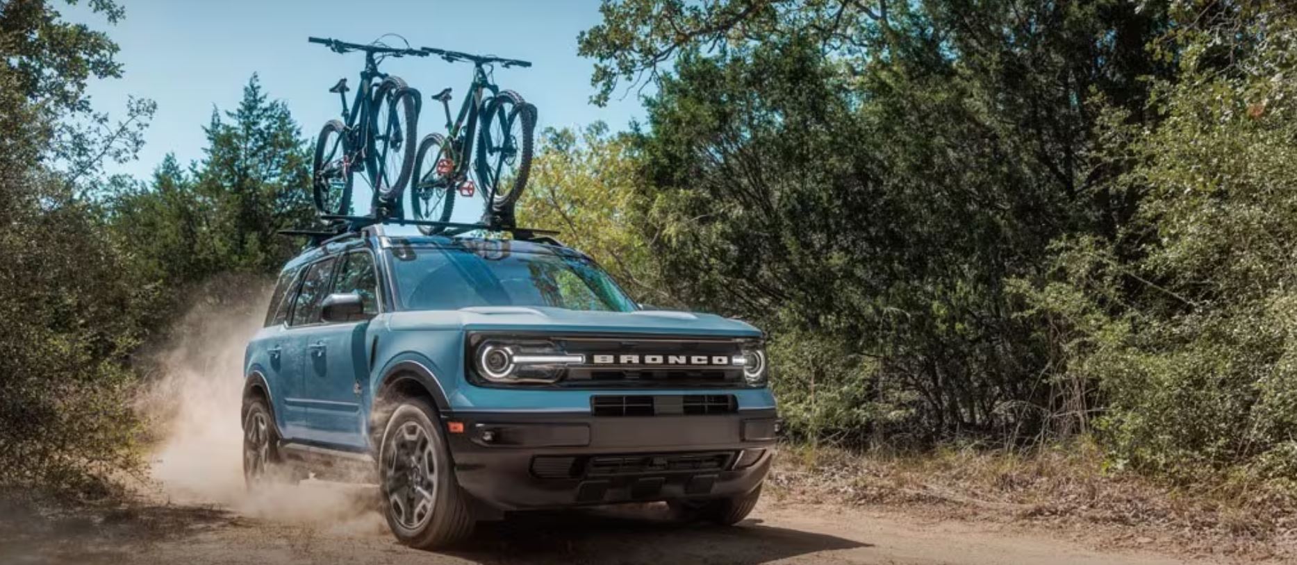 2024-ford-bronco-sport-1.JPG A blue 2024 Ford Bronco Sport driving on a dirt road with mountain bikes mounted to the roof drives toward the viewer