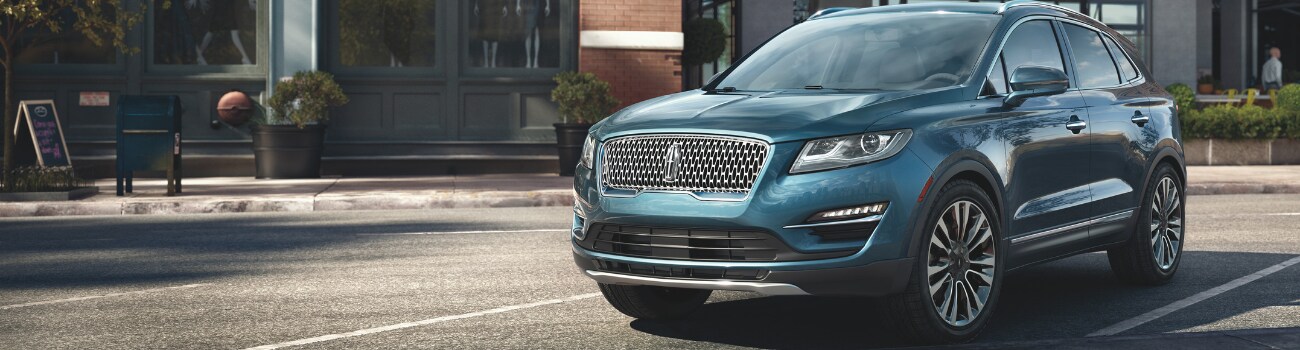 2019 Lincoln MKC price in Colorado Springs at Phil Long Lincoln.png Front driver side angle of a 2019 Lincoln MKC luxury SUV with a metallic glossy finish shining in the sun parked outside a modern building in Colorado Springs