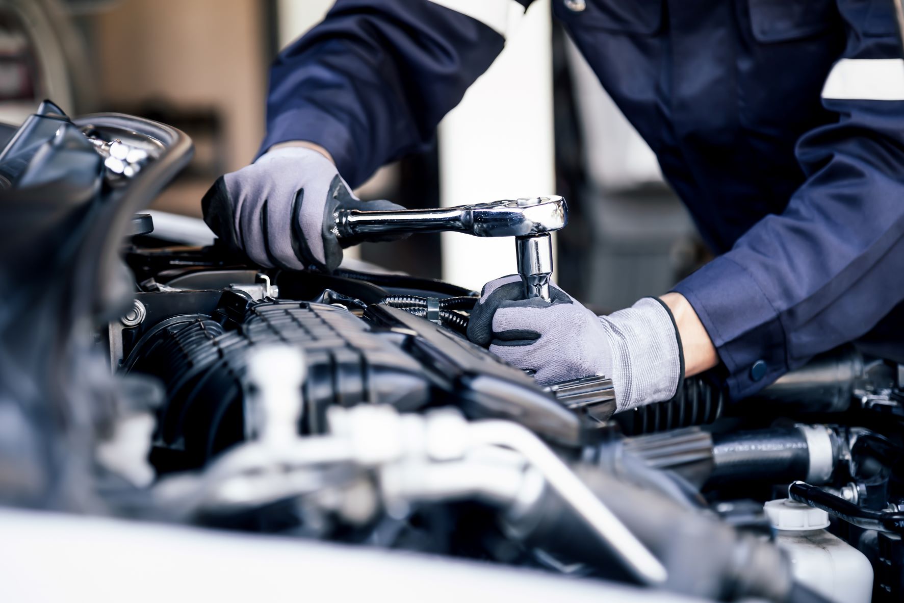 AdobeStock_440519588.jpeg A mechanic tightening a nut inside of the hood of a Lincoln.