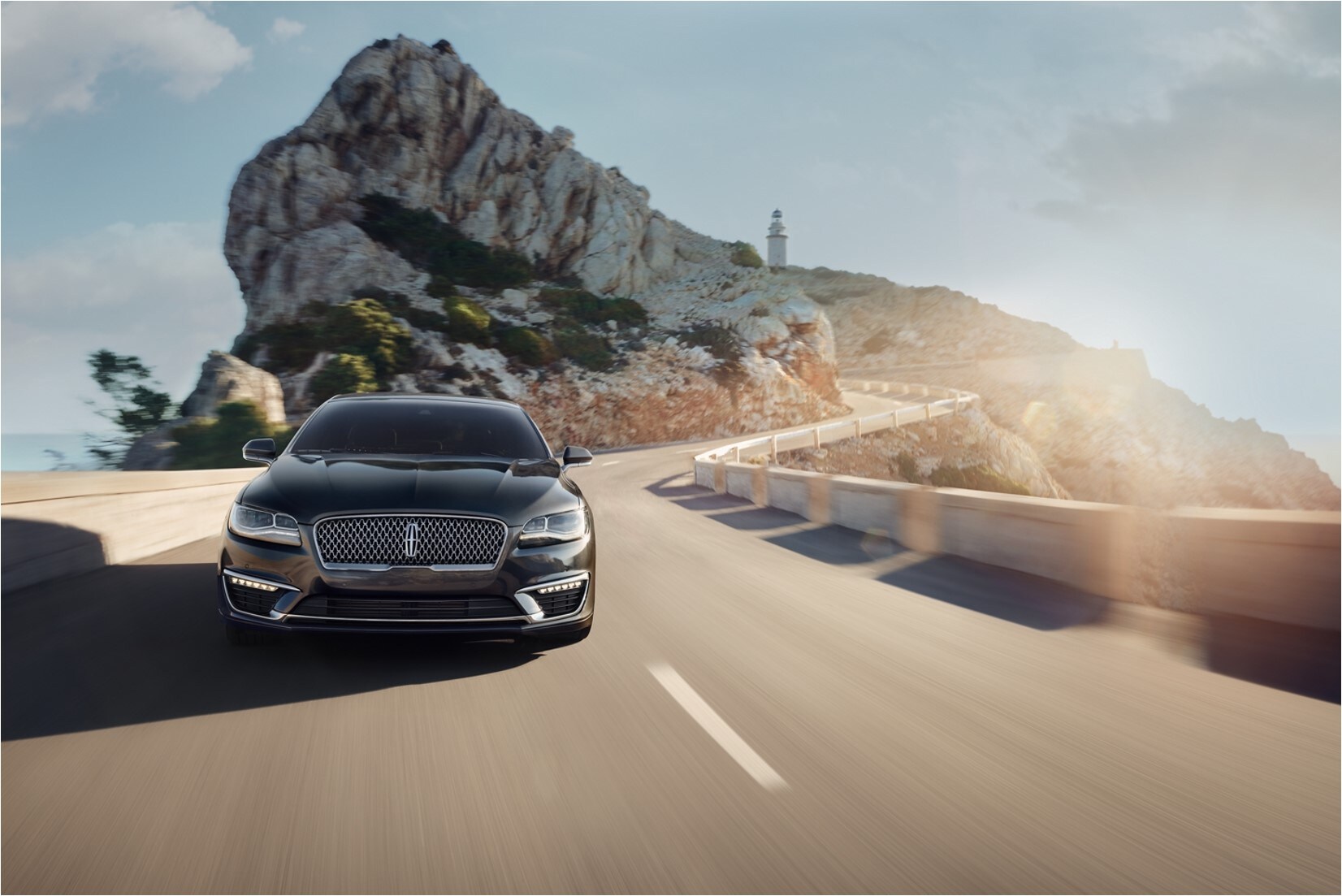 2020-lincoln-mkz-phil-long-lincoln-colorado.jpg A 2020 Lincoln MKZ driving on a scenic road with ocean rocks and a lighthouse in the distance