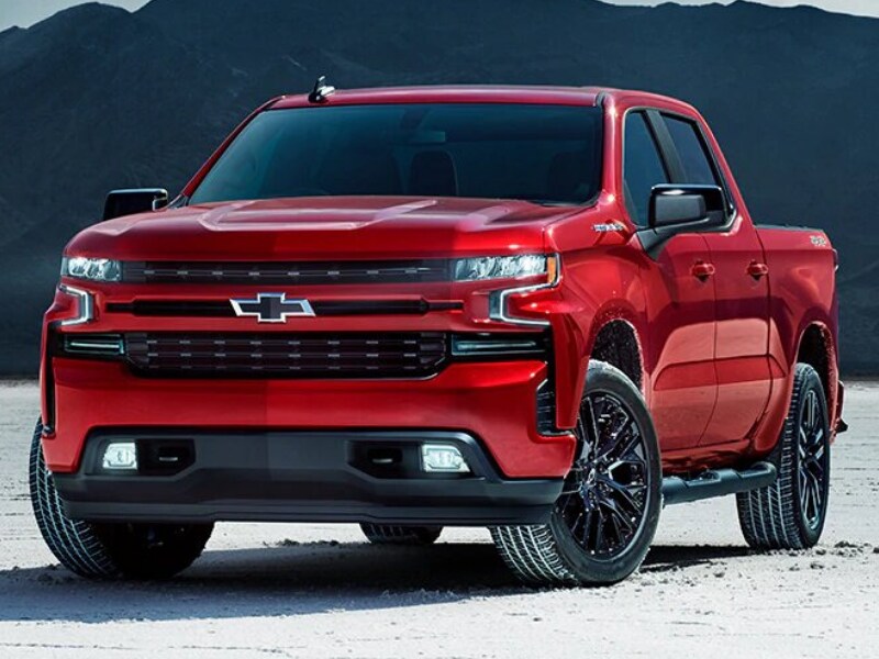 Exterior view of a 2019 Chevy Silverado parked in a sandy field in front of mountains